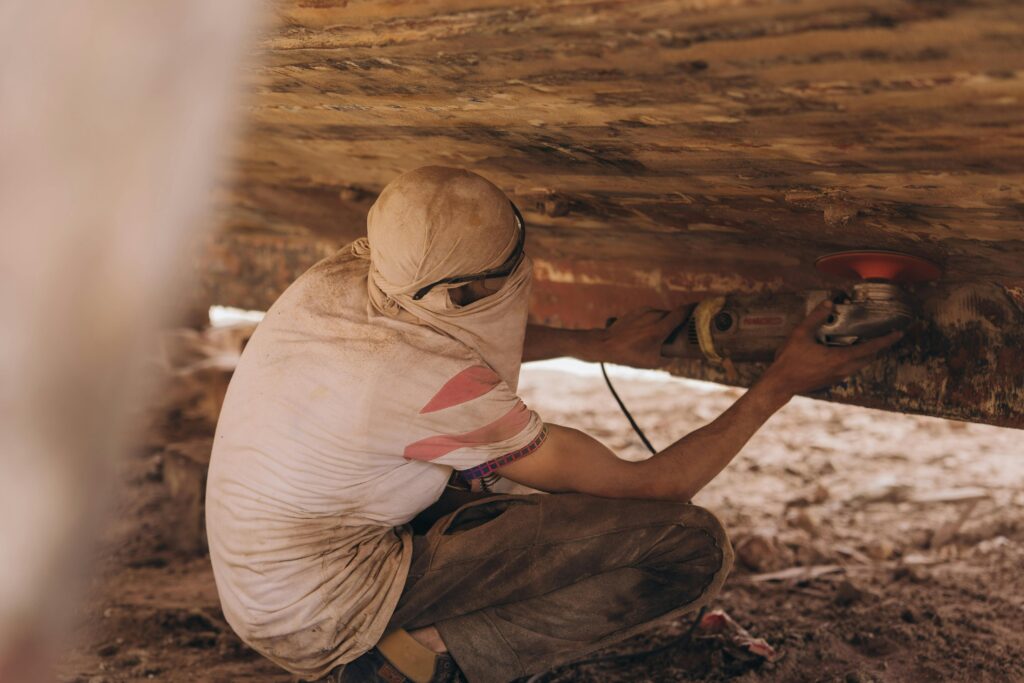 Man sandblasting under a boat in Kafr El-Shaikh, Egypt, depicting hard work and craftsmanship.